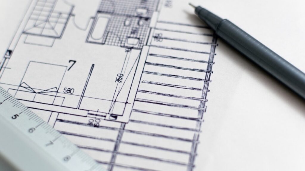 A scale ruler and pen resting on a floor plan with room dimensions marked